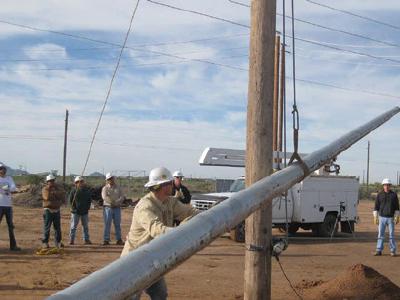 Workers positioning steel utility pole with crane